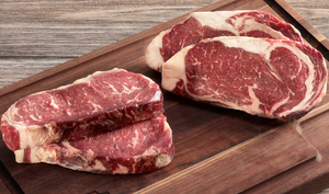Two uncooked Dry aged ribeyes and two uncooked dry aged New York strip steaks on a cutting board
