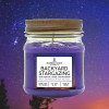 a candle in a clear glass mason jar with purple wax and a label that reads "Backyard Stargazing" against a starry night sky